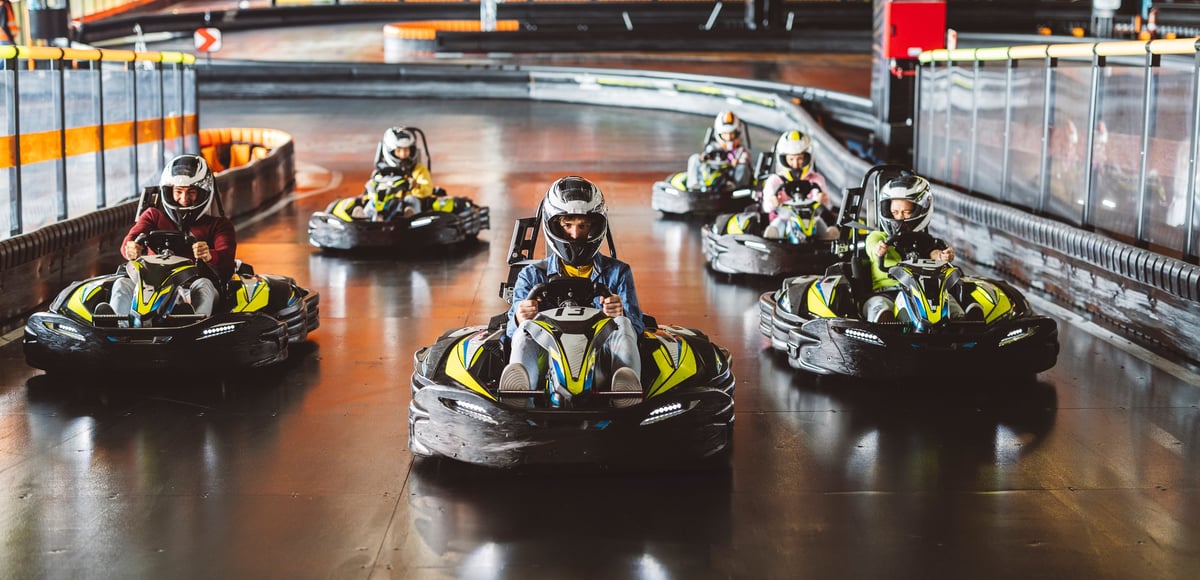 A racer in a helmet leads the pack through a turn on the indoor electric karting track at AFTERSHIFT