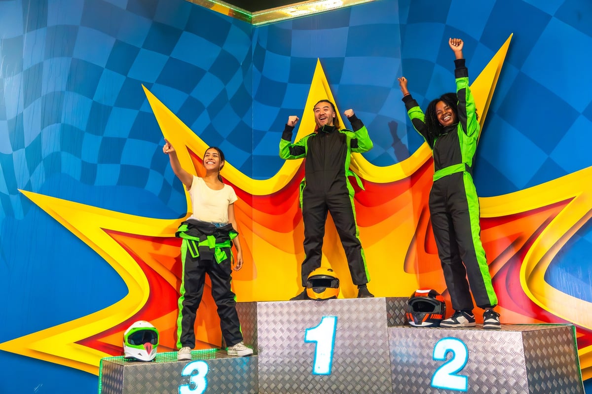A group of friends in racing suits and helmets celebrating together on the indoor karting podium