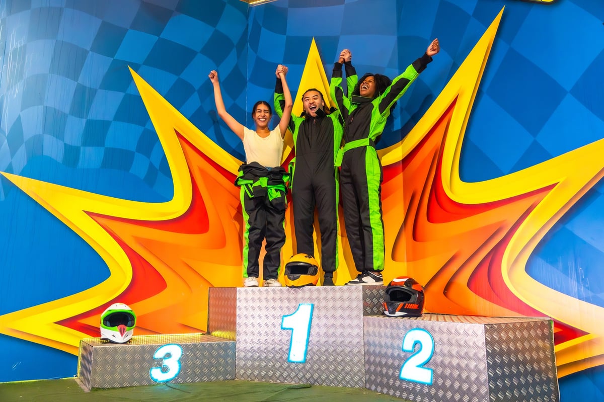 Three friends raising their arms on the karting victory podium after a race
